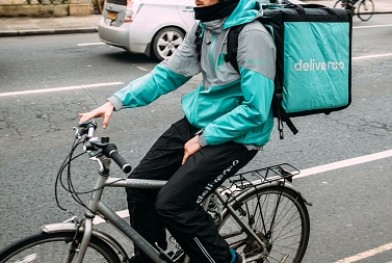 Oxford_United_Kingdom_Mar_3_3017_Side_view_of_young_male_cyclist_delivering_food_fast_to_client_via_Deliveroo_App_commuting_fast_in_the_university_city_with_big_thermo_bag_with_Deliveroo_logo